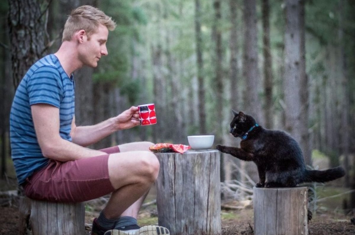 Mann und seine Katze sitzen an einem Baumstamm